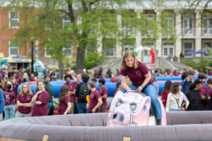 A University of Mary Washington student hangs onto a mechanical pig. Devils vie for points against Goats during the uniquely Mary Washington tradition of Devil-Goat Day. Photo by Parker Michels-Boyce.