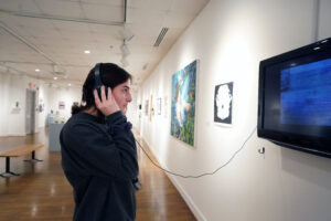 A visitor inside UMW's duPont art gallery listens to a multimedia installation at the Student Art Exhibit, on view during Research and Creativity Day. Photo by Suzanne Carr Rossi.