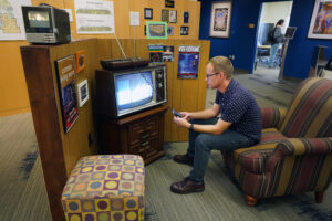 Associate Professor of Communication and Digital Studies Zach Whalen makes adjustments to a 1980s-era Intellivsion gaming console. The partial display, on view as part of the 'A Decade of Digital Convergence' exhibit, pays homage to the Console Living Room, once a popular area inside the Hurley Convergence Center that, at separate times, represented a living room from the 1980s and '90s. Photo by Suzanne Carr Rossi.