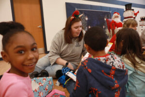 The combination of gifts and holiday magic created moments of pure delight for the preschoolers, pictured with UMW student Sarah Hybl '25. Photo by Karen Pearlman.