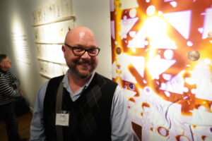 One of Garmon's first students, Tom Condon (VA Tech ’00), poses with his artwork on display in the duPont Gallery through March 23.