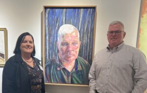 Trenchard and her husband, Terry, pose with the portrait named after him, which was displayed in the UMW Galleries as part of the Mid-Atlantic New Painting Biennial, which ran Nov. 7, 2024, through Jan. 19, 2025. Photo courtesy of Kathleen Trenchard.